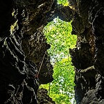 Limestone cave opening with lush green trees visible from inside.