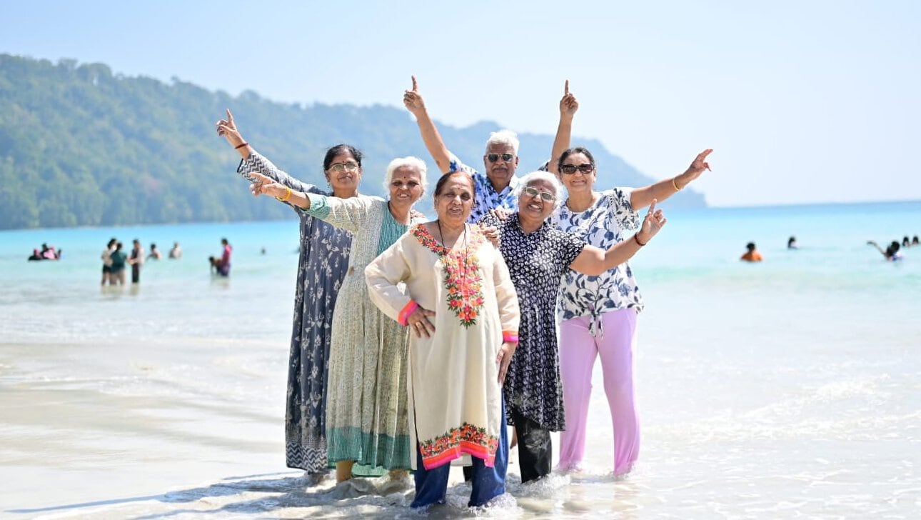 Senior women celebrating on the beach in Andaman with clear blue water and lush green hills.