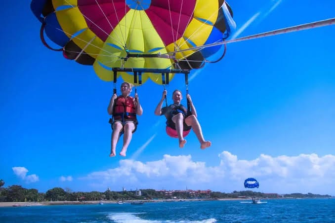 Tourists enjoying parasailing over the turquoise waters of the Andaman Islands with breathtaking aerial views of the coastline and beaches.