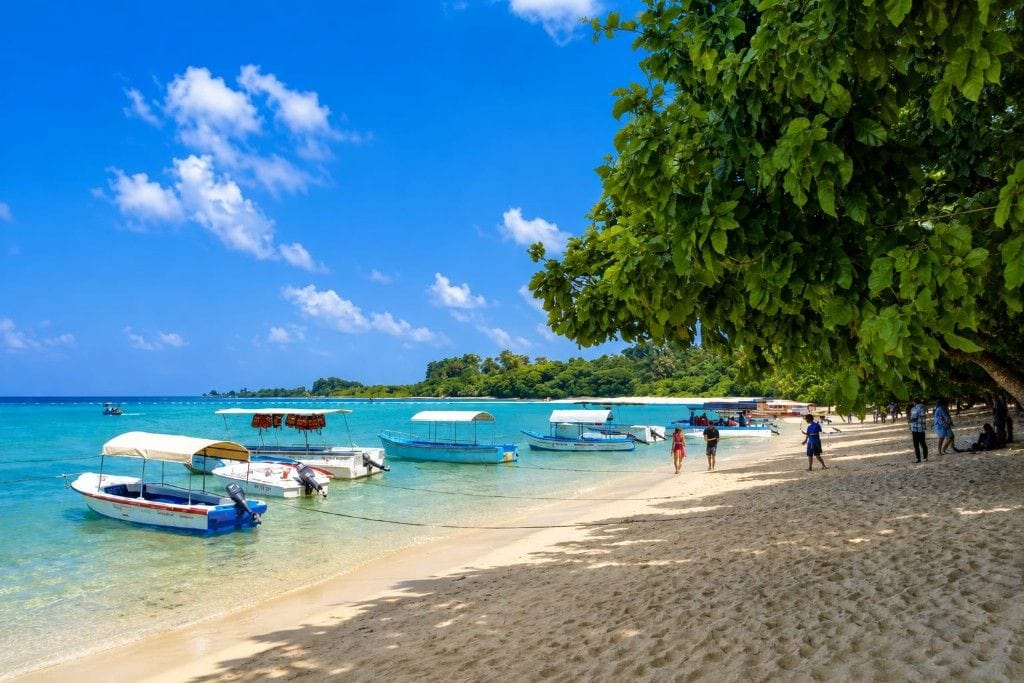 Beautiful Andaman beach with boats, clear blue water, and lush green trees.