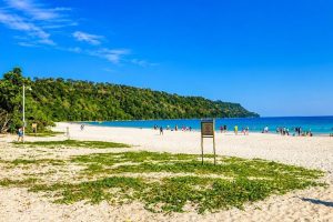 Beautiful Andaman beach with white sand, clear blue water, and lush green hills.