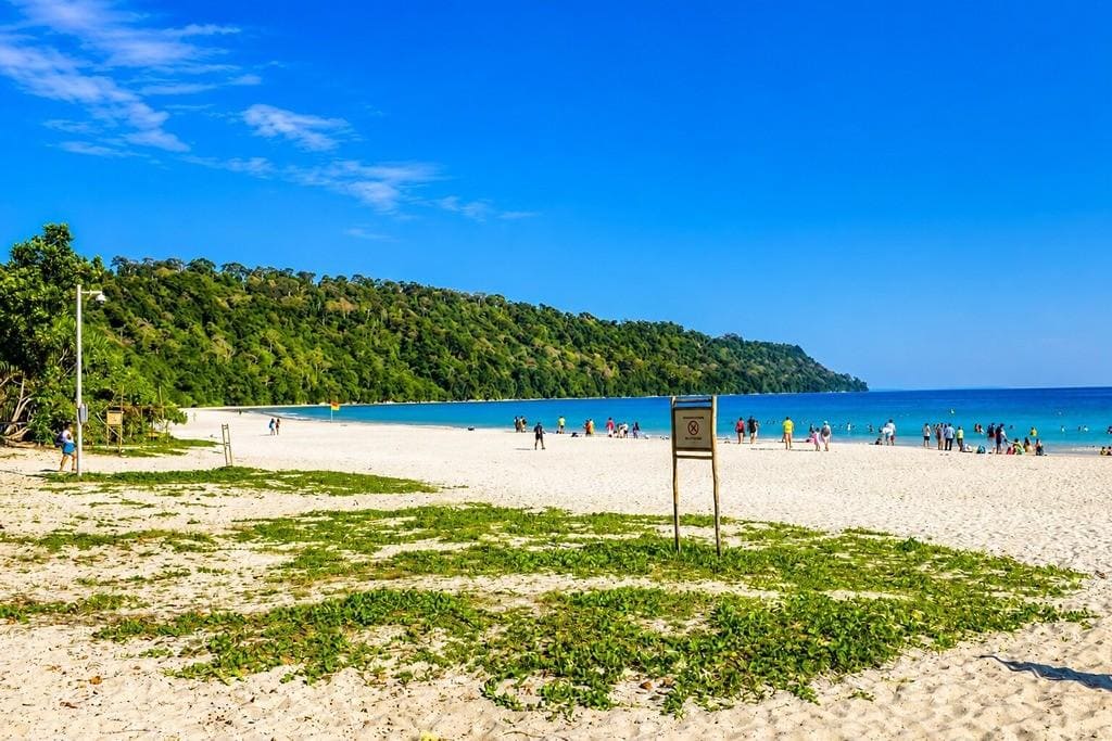 Beautiful Andaman beach with white sand, clear blue water, and lush green hills.