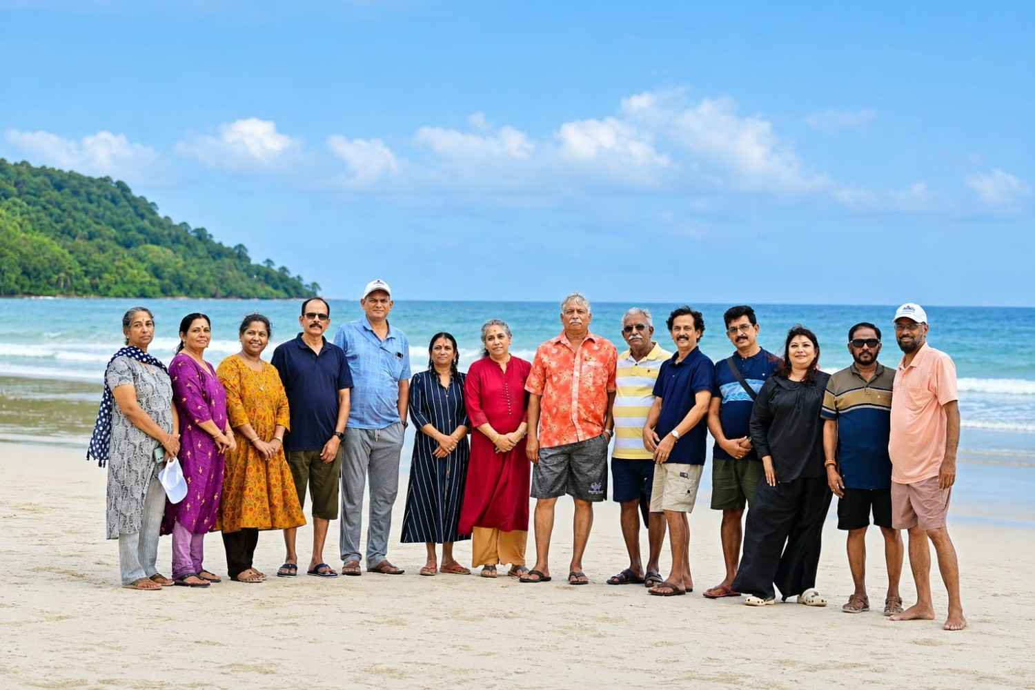 Group of tourists on the beach in Andaman Islands with lush green hills in background.