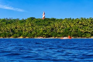 Lighthouse on lush tropical island with blue sea and sky.