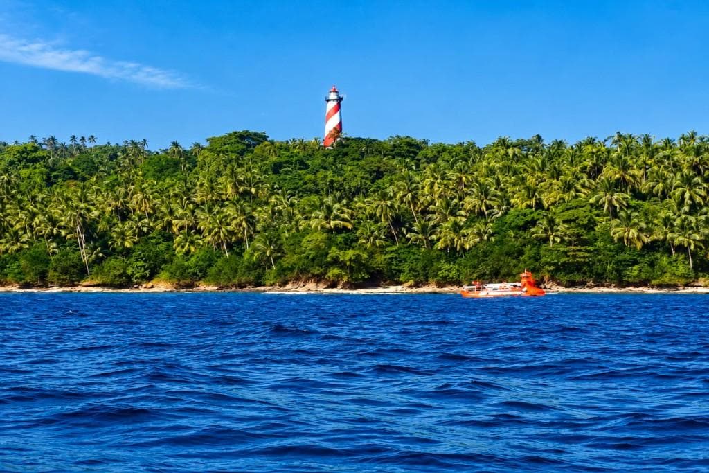 Lighthouse on lush tropical island with blue sea and sky.